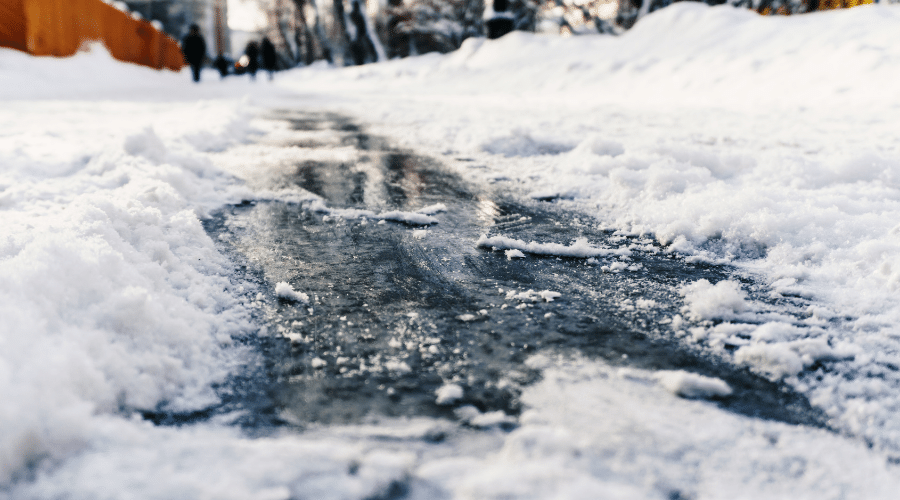 Slippery sidewalk due to drainage issues and freezing weather, which is a safety hazard for pedestrians