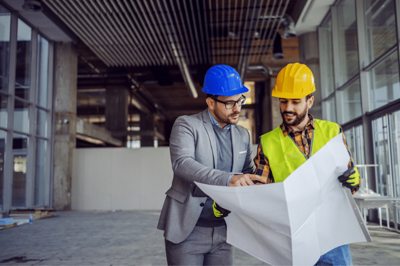 Engineer and construction professional reviewing project plans at an active building site, demonstrating coordination between design and construction teams during project development.