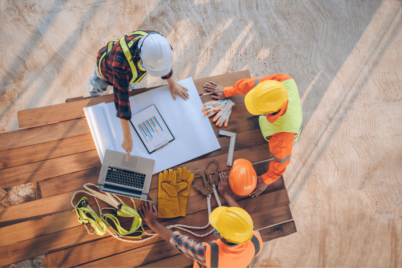 Project team reviewing plans, schedules, and construction documents at a job site, illustrating collaboration between engineering, design, and construction professionals.