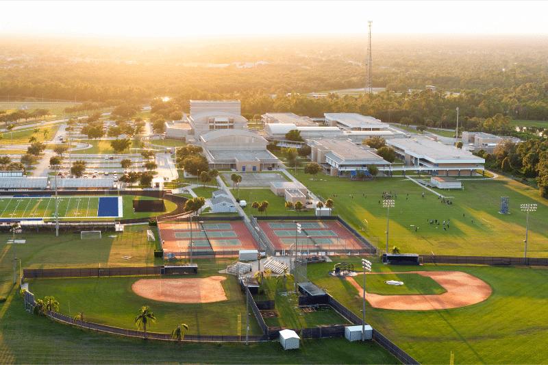 Aerial view of a school campus with academic buildings, parking areas, pedestrian paths, athletic fields, tennis courts, and baseball fields.