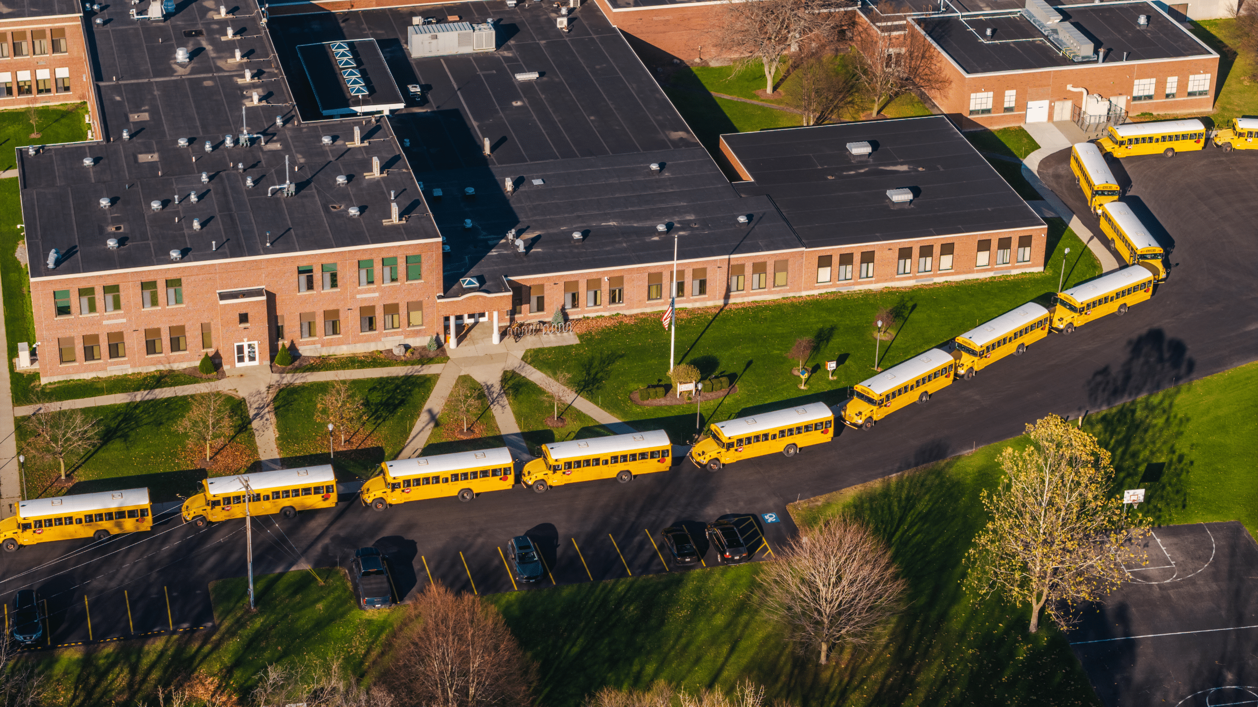 Aerial view of a school campus with school buses, parking areas, sidewalks, and surrounding site infrastructure.