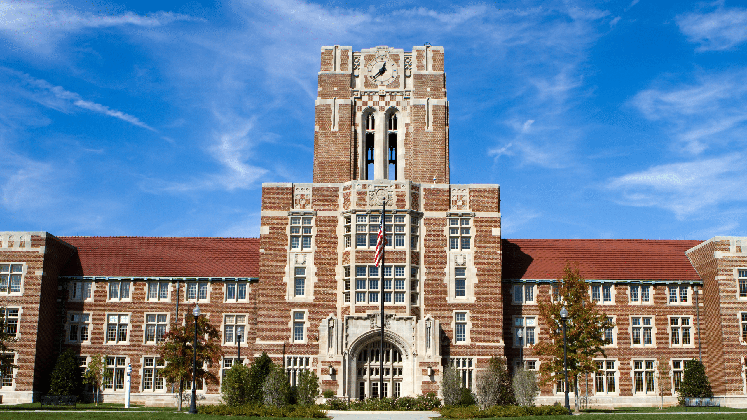 Historic brick school building with a central clock tower and American flag under a bright blue sky.